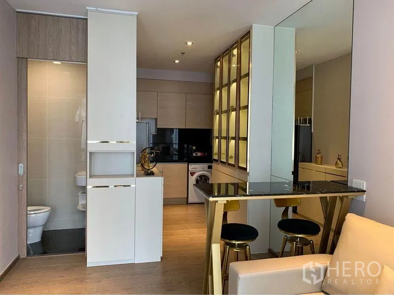 Condominium for sale - Modern kitchenette with built-in cabinets, black backsplash, washing machine and adjacent bathroom.