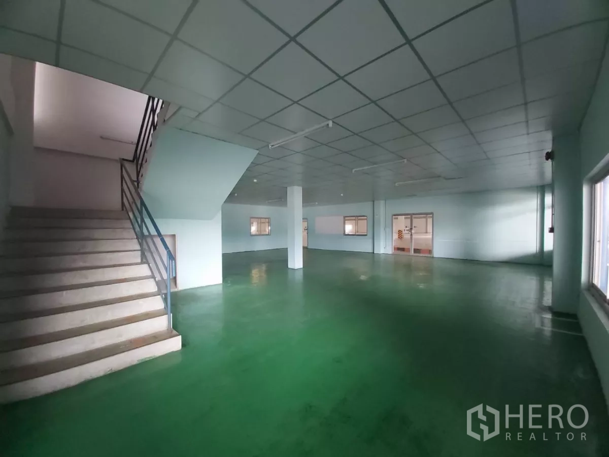 Warehouse for rent in Bang Bo, Samut Prakan - Ground-floor office hall with green epoxy flooring and a staircase.