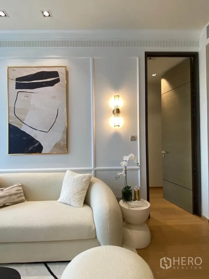 公寓 for rent in Pathum Wan, Bangkok - 客厅一角配米色沙发、墙面装饰画与壁灯，旁置小边几与花卉。