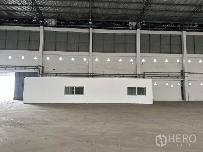 Factory for rent in Bang Bua Thong, Nonthaburi - Interior wall with built‑in office module and windows inside the warehouse.
