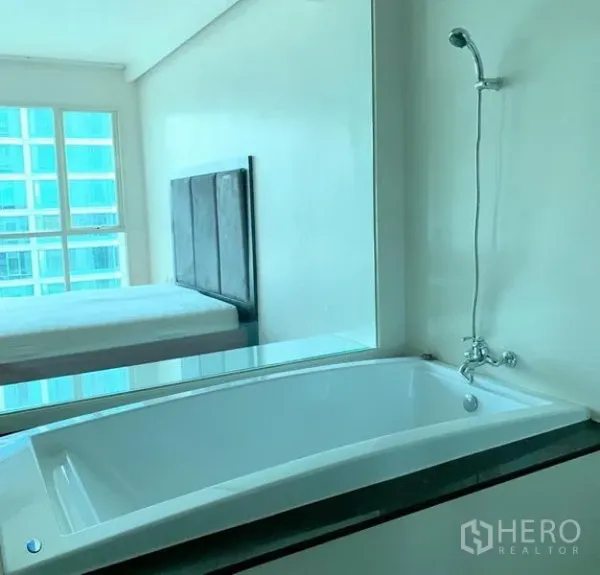 Condominium for rent in Pathum Wan, Bangkok - Bathroom with soaking bathtub and glass panel overlooking the bedroom, offering high-rise views.