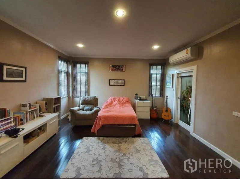 Detached House for sale in Sai Mai, Bangkok - Cozy bedroom with wood flooring, armchair, bookshelves and air conditioner.