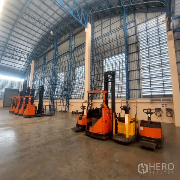 Warehouse for rent in Mueang Pathum Thani, Pathum Thani - Electric forklifts and pallet jacks parked under tall steel truss walls inside the warehouse.