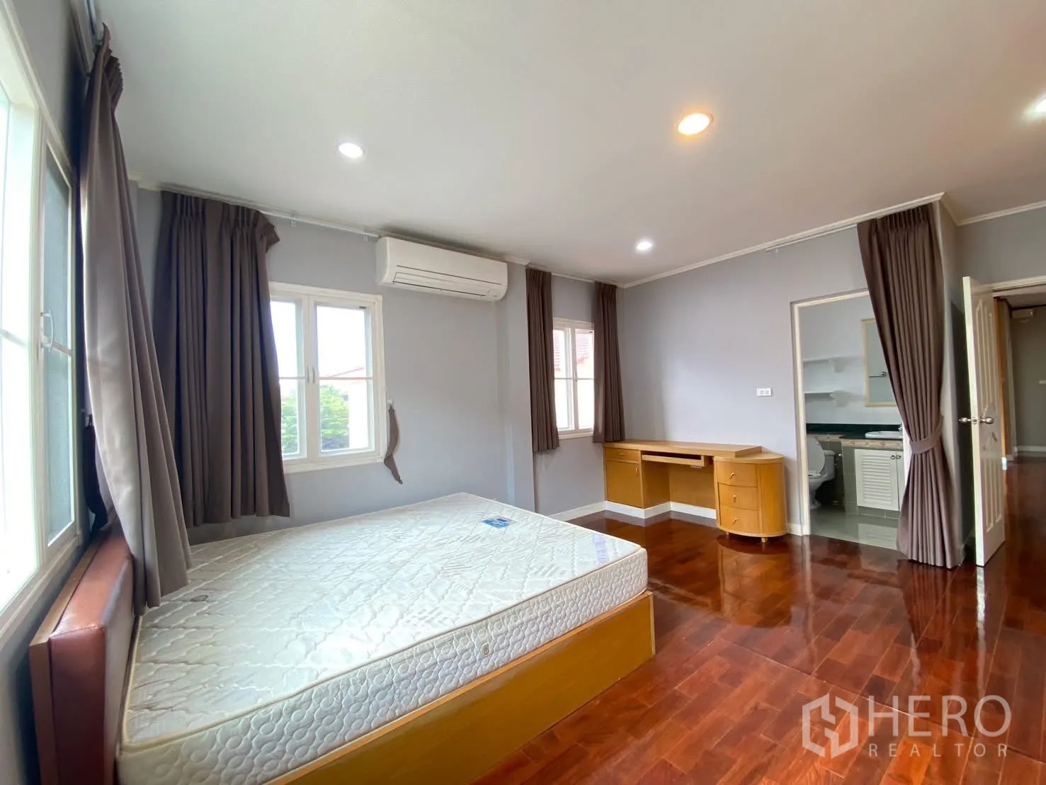 Detached House for rent in Phra Khanong, Bangkok - Bright bedroom with hardwood floor, built-in desk, windows, air conditioner, and an ensuite bathroom visible.