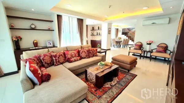 Apartment for rent in Watthana, Bangkok - Bright living room with L-shaped sofa, patterned cushions, rug and built-in shelving in a Watthana apartment.