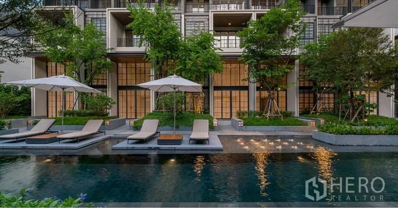联排别墅 出租在Watthana, Bangkok - 度假风泳池配躺椅与遮阳伞，前方是绿意环绕的现代联排别墅外立面