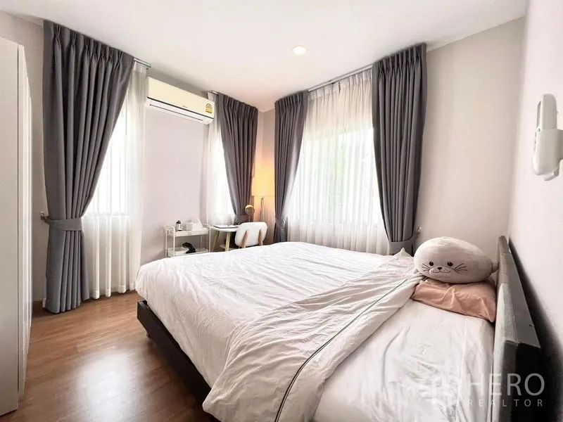 Detached House for rent or sale in Bang Khen, Bangkok - Corner bedroom with white bedding, study desk, air conditioner and double windows.