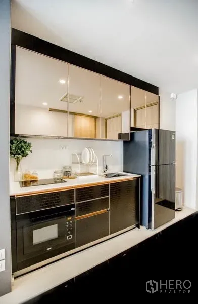 Condominium for rent in Pathum Wan, Bangkok - Compact modern kitchen with glossy cabinets, built-in microwave, sink, and full-size fridge.