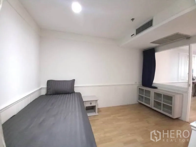 Condominium for rent in Khlong Toei, Bangkok - Guest bedroom with single bed, side table, and low storage cabinet beneath the window.