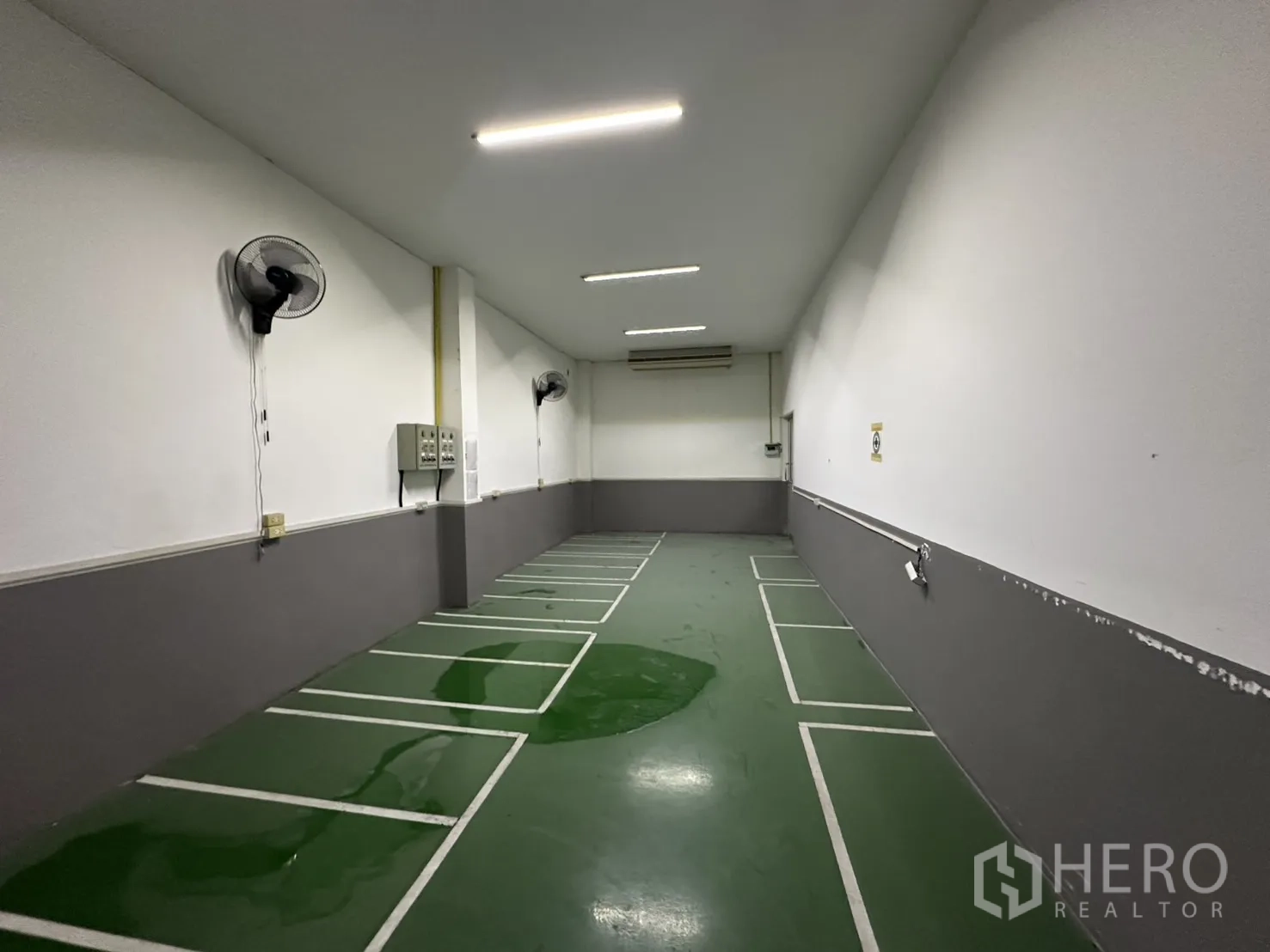 工厂 出租 - 狭长绿色地坪房，墙式风扇与划线工位。