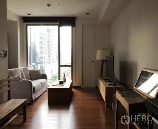 Condominium for rent or sale in Khlong Toei, Bangkok - Open-plan lounge with TV cabinet and floor-to-ceiling window overlooking city buildings and greenery.
