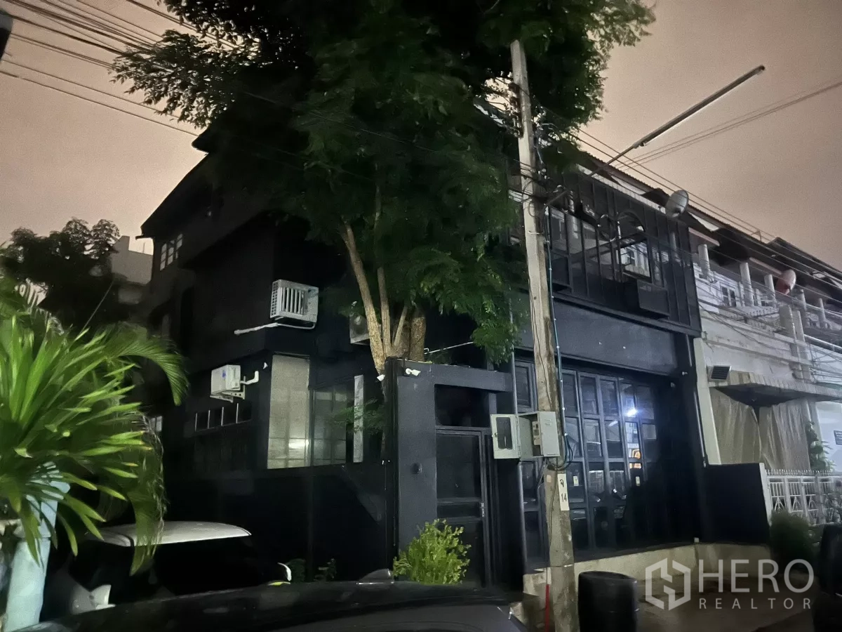 带办公室的家 出租在Wang Thonglang, Bangkok - 夜间建筑外观，树木与玻璃门面清晰可见。