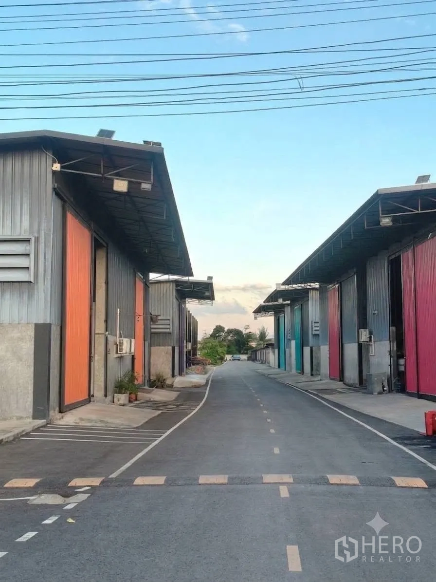 โกดัง for rent in Bang Bua Thong, Nonthaburi - ถนนภายในโครงการปูแอสฟัลต์ มีโกดังเรียงราย สายไฟเหนือศีรษะ และลูกระนาด