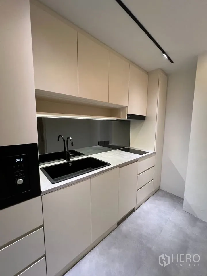 联排别墅 for rent in Prawet, Bangkok - 一字型厨房，米色橱柜、黑色水槽和电磁炉。