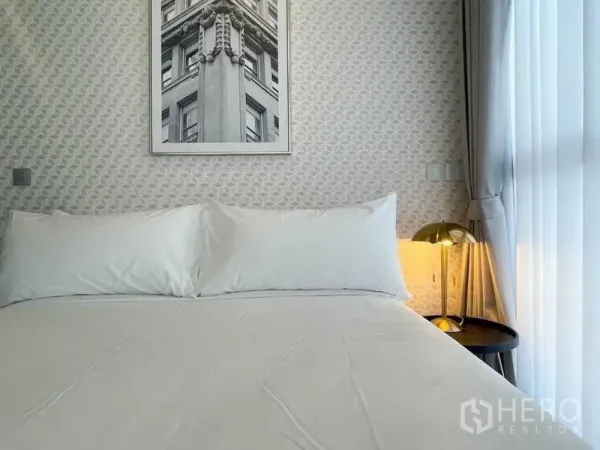 公寓 出租在Ratchathewi, Bangkok - 近景：床铺与几何墙纸，金色床头灯与落地纱帘，简洁雅致。