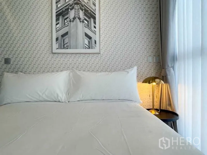 公寓 出租在Ratchathewi, Bangkok - 近景：床铺与几何墙纸，金色床头灯与落地纱帘，简洁雅致。