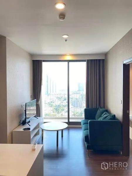 คอนโด ให้เช่า - ห้องนั่งเล่นสว่างที่ Whizdom Inspire Sukhumvit 101 มีหน้าต่างเต็มบาน โซฟา ชั้นวางทีวี และวิวเมืองจากระเบียง