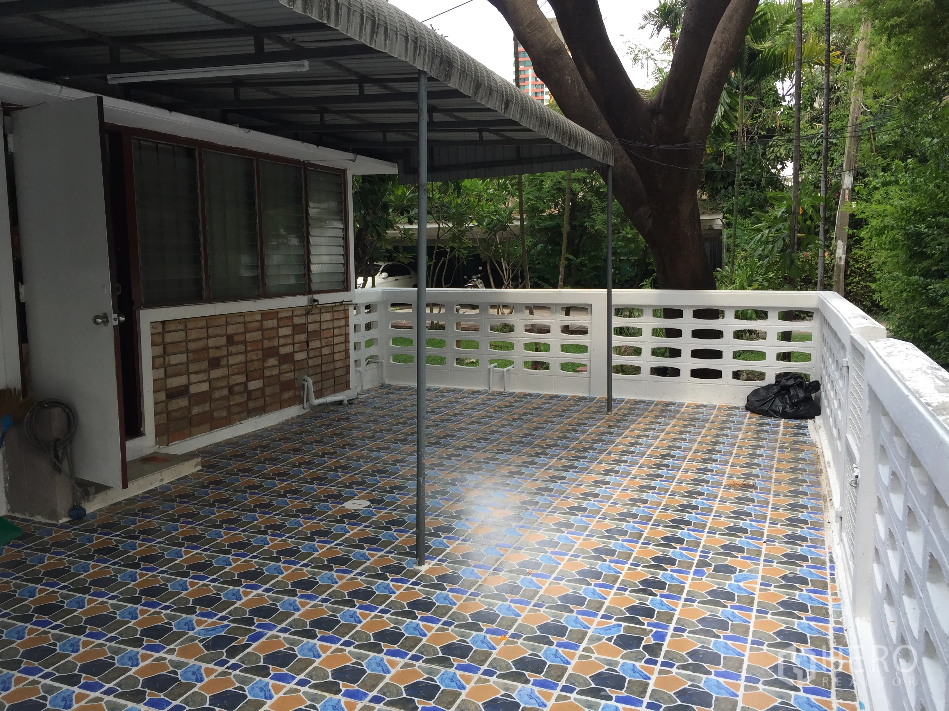 Townhouse for rent in Yan Nawa, Bangkok - Large tiled terrace with awning and white railing facing a green garden.