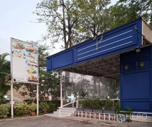 零售空间 出租在Bueng Kum, Bangkok - 转角店铺外立面，蓝色招牌、透明雨棚与绿植