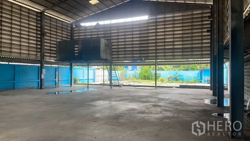 Warehouse for rent in Bang Na, Bangkok - Wide clear-span warehouse with skylights and ventilation louvers facing a fenced outdoor area.
