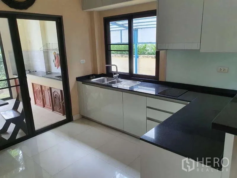 独立式住宅 出租在Mueang Nonthaburi, Nonthaburi - 明亮西式厨房，黑色花岗岩台面、白色橱柜与滑门通往泰式厨房。