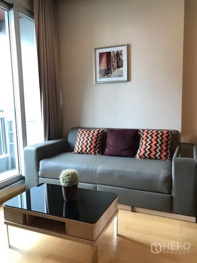 Condominium for rent in Ratchathewi, Bangkok - Bright living room with gray sofa, glass coffee table and balcony sliding doors.