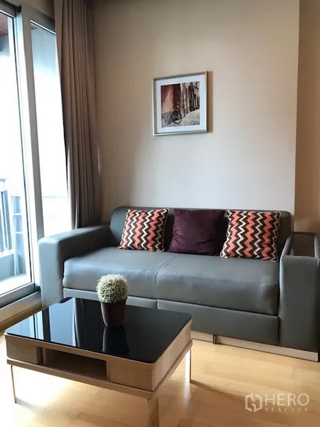 Condominium for rent in Ratchathewi, Bangkok - Bright living room with gray sofa, glass coffee table and balcony sliding doors.