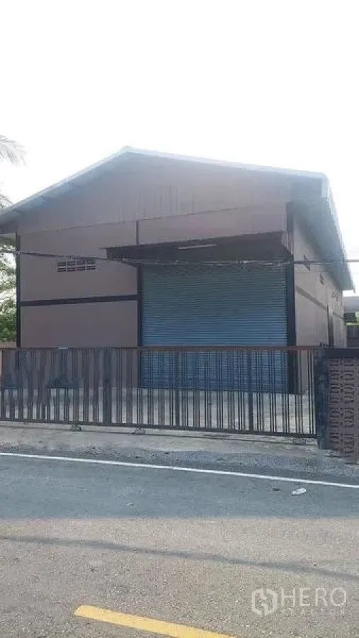 货栈 出租在Pathum Thani - 临街仓库立面，带大幅蓝色卷闸门与围栏大门。