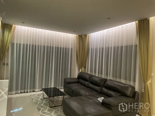 Detached House for rent or sale in Lam Luk Ka, Pathum Thani - Cozy lounge corner with floor-to-ceiling sheer curtains, leather sofa and marble coffee table.
