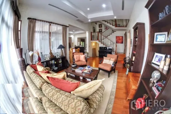 Detached House for rent in Watthana, Bangkok - Open-plan lounge with sofa set, bookshelves and a statement wooden staircase.