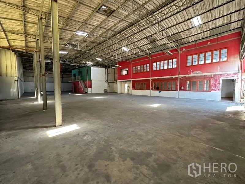 货栈 出租在Suan Luang, Bangkok - 开阔工业空间，钢桁架与采光窗，上侧为红色办公室。