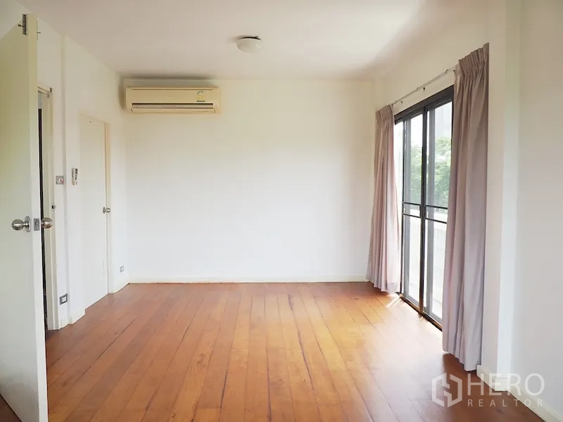 Detached House for rent in Chatuchak, Bangkok - Empty bedroom with wood floors, air-conditioning, and balcony access.