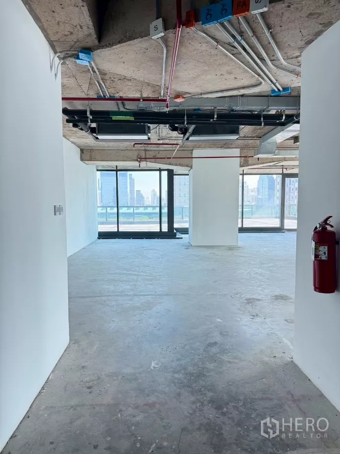 Office Space for rent in Din Daeng, Bangkok - Unfurnished office floor with concrete slab, visible fire-safety piping, and wide glazing toward a balcony.