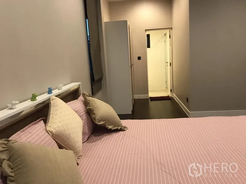 Detached House for rent in Bang Kapi, Bangkok - Cozy bedroom with pink bedding leading to an ensuite bathroom via a short corridor.