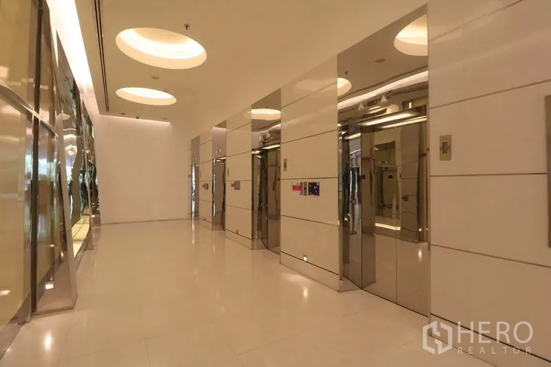 Office Space for rent in Bang Rak, Bangkok - Modern elevator lobby with multiple stainless-steel lifts and circular recessed ceiling lights.