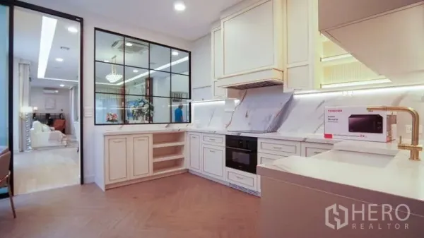 Detached House for rent in Saphan Sung, Bangkok - Modern L-shaped kitchen with marble backsplash, cream cabinets and a glass partition to the dining area.