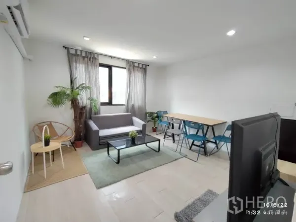 Home Office for rent - Bright living and work area with gray sofa, glass coffee table, long desk with blue chairs, window and indoor plants.