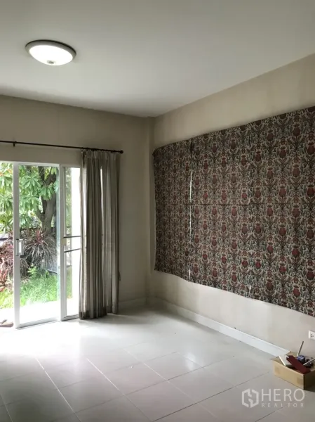Detached House for rent in Lat Krabang, Bangkok - Bright living room with white tile floors, sliding glass doors and curtains opening to a green garden.