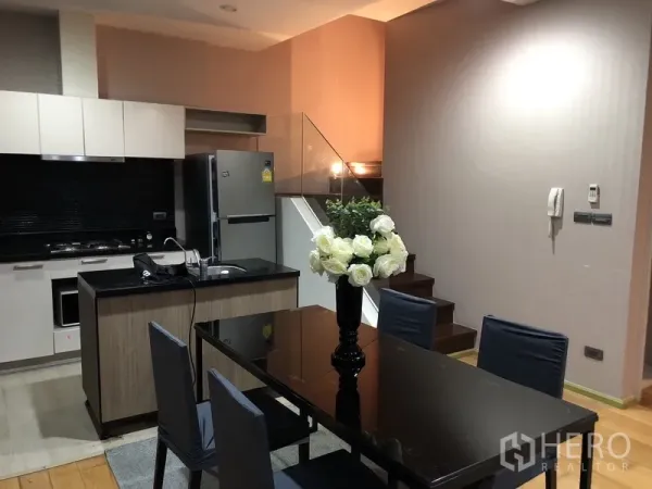 公寓 出租或出售在Khlong San, Bangkok - 现代厨房，黑色石材台面、白色柜体，旁边是玻璃扶手楼梯与餐桌。