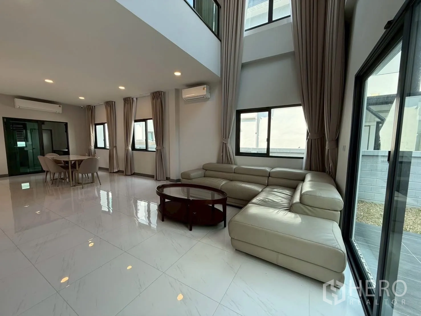 Townhouse for rent - Spacious living and dining room with large white tiles, multiple windows and a sectional sofa.