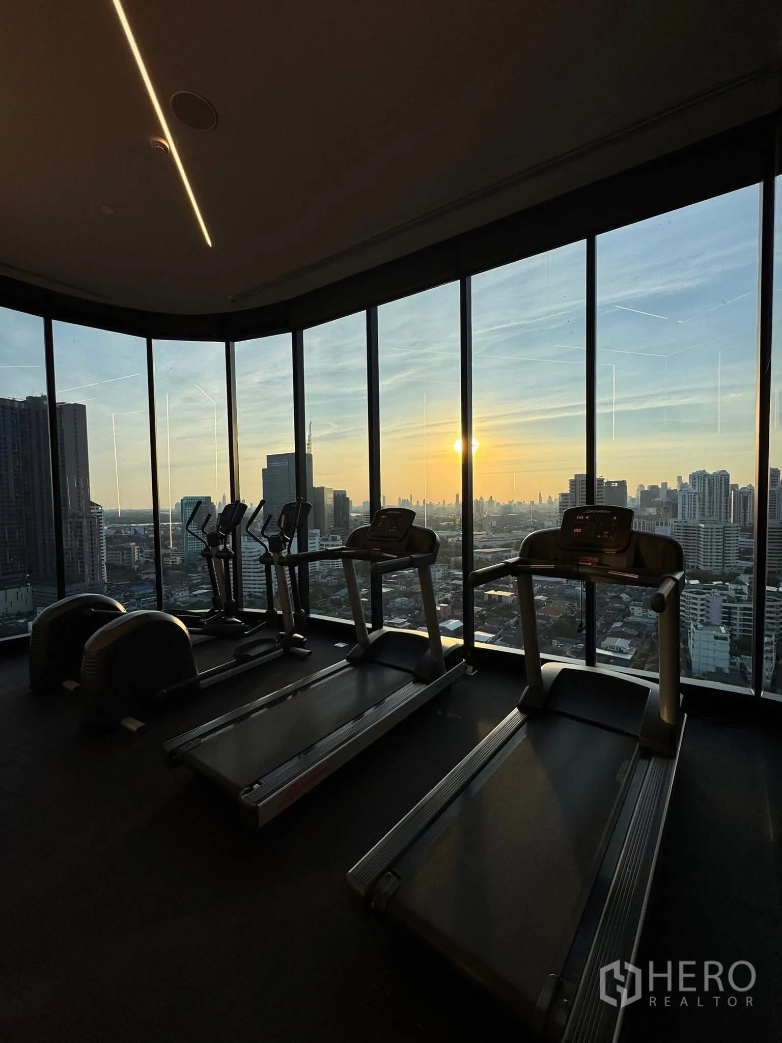 Condominium for rent in Khlong Toei, Bangkok - High-floor fitness center with treadmills facing a panoramic Bangkok sunset skyline.