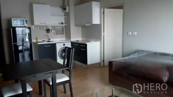 Condominium for rent in Watthana, Bangkok - Compact kitchen with refrigerator, microwave, washing machine and dining set beside a sofa in an Ekkamai condo.