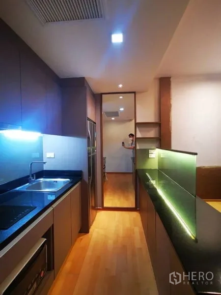 Condominium for sale in Khlong Toei, Bangkok - Galley kitchen with granite counters, sink, cooktop and under-cabinet lighting.