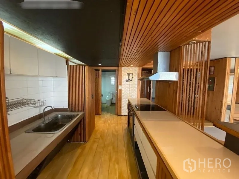 Condominium for rent or sale in Suan Luang, Bangkok - Galley kitchen with long countertops, sink, cooktop and doorway to a bathroom.