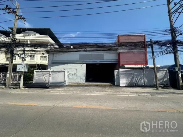 货栈 出租在Suan Luang, Bangkok - 面向街道的仓库，金属推拉门与宽阔门面，电线横跨上方。