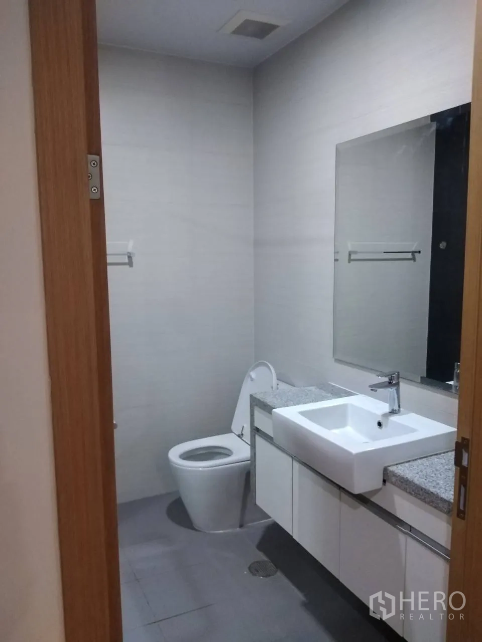 Condominium for rent in Khlong Toei, Bangkok - Modern bathroom with square basin, granite countertop, large mirror, and toilet.