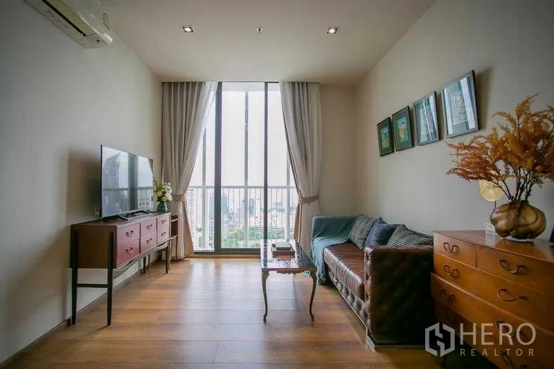Condominium for sale in Khlong Toei, Bangkok - Cozy living room with TV console and sofa facing a tall window with city skyline view.