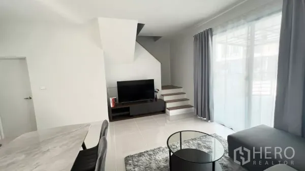 Townhouse for rent in Bang Phli, Samut Prakan - Bright living area with TV console, staircase and floor-to-ceiling sliding doors with curtains.