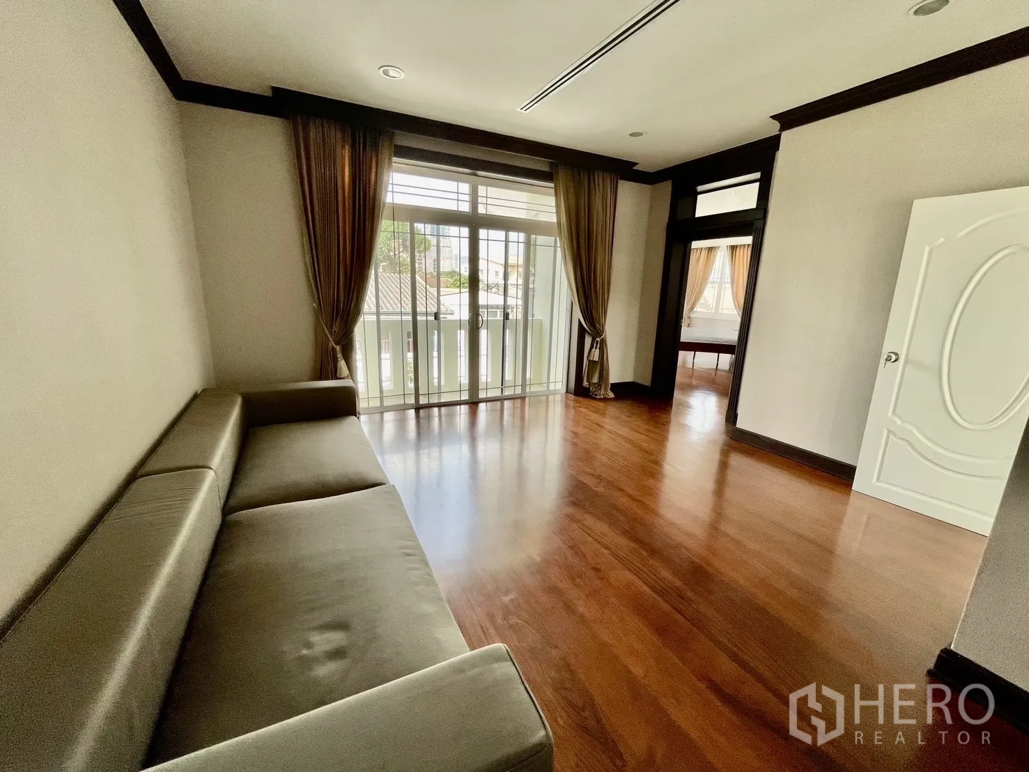 Detached House for rent in Chatuchak, Bangkok - Upstairs family room with sofa and balcony doors over wooden flooring.