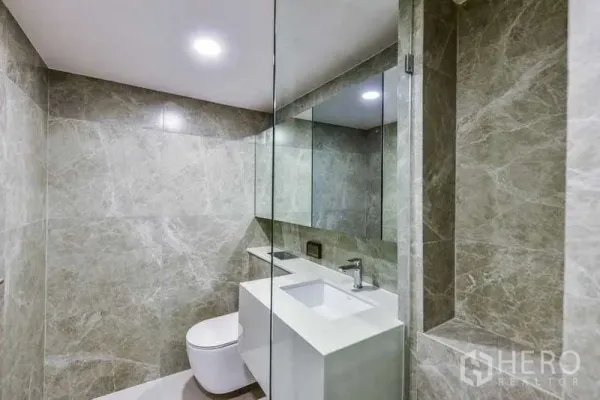 Condominium for rent in Huai Khwang, Bangkok - Modern bathroom with marble-look tiles, large mirror and white vanity.